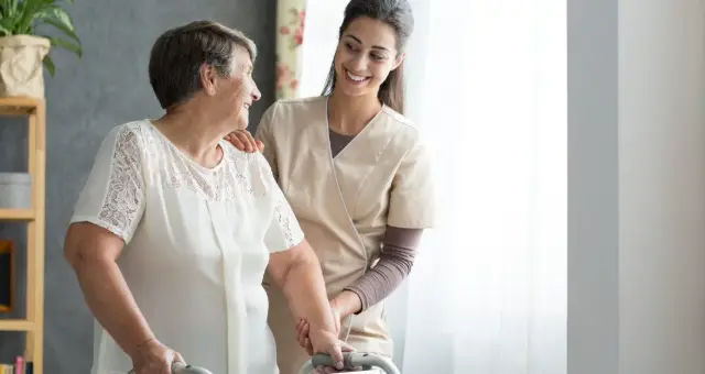Nurse helping an older woman walk with a frame