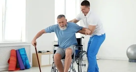 Carer supporting a man in a wheelchair at home