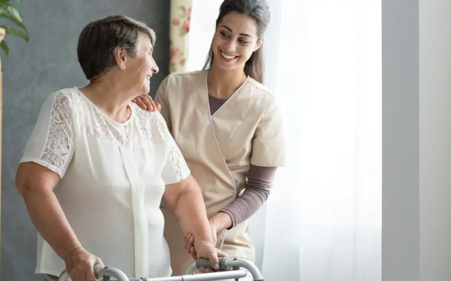 Nurse helping an older woman walk with a frame