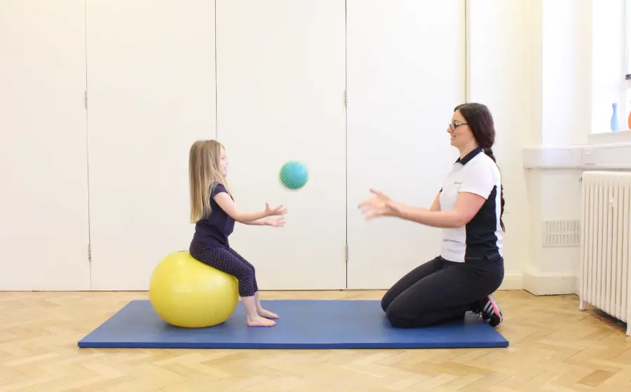 Physiotherapist doing a ball exercise with a child on a mat